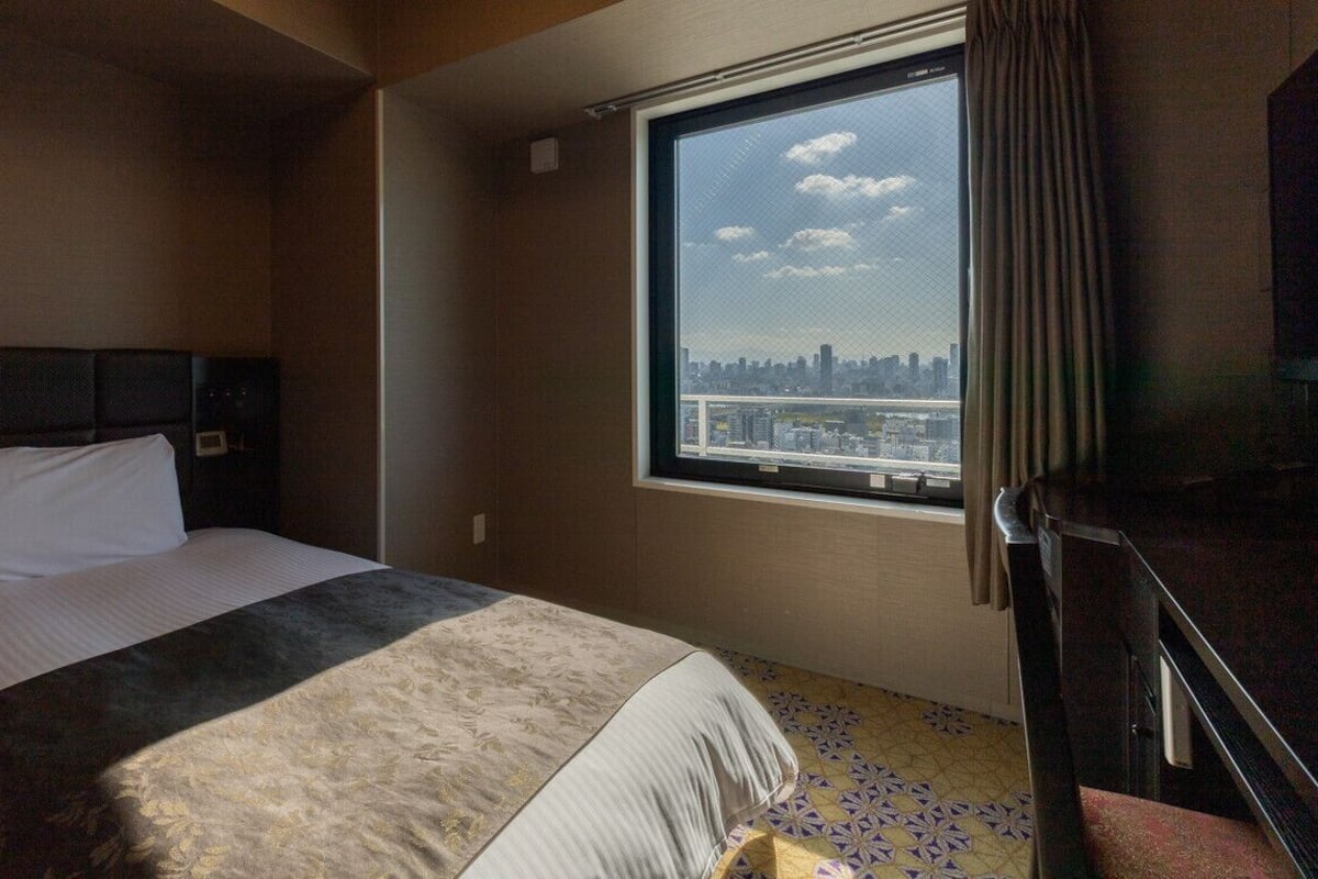 Une chambre d’hôtel avec un lit, une fenêtre donnant sur la ville et une porte.