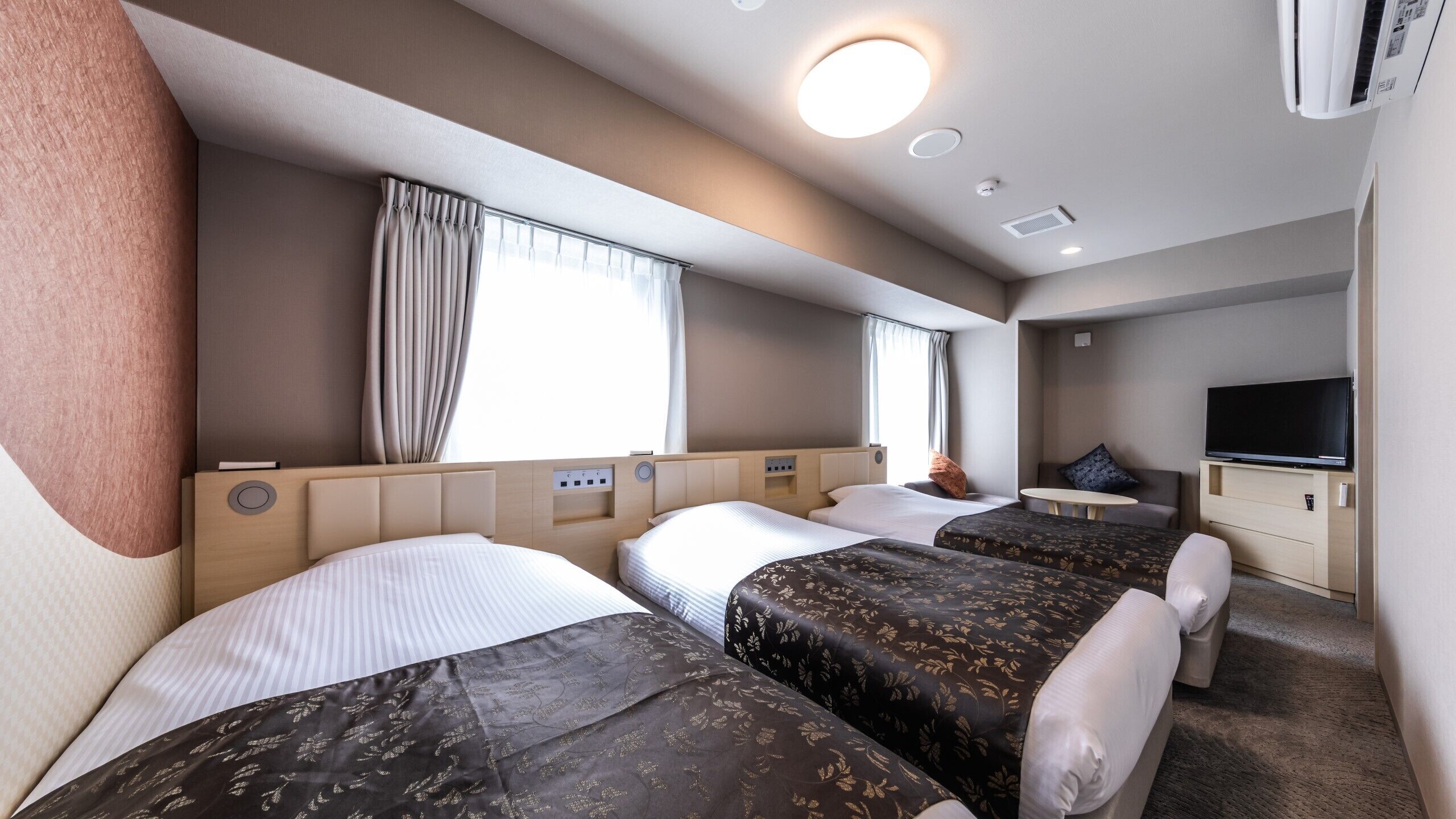 Ein Hotelzimmer mit drei Betten, einem Fernseher und einer kleinen Sitzecke.