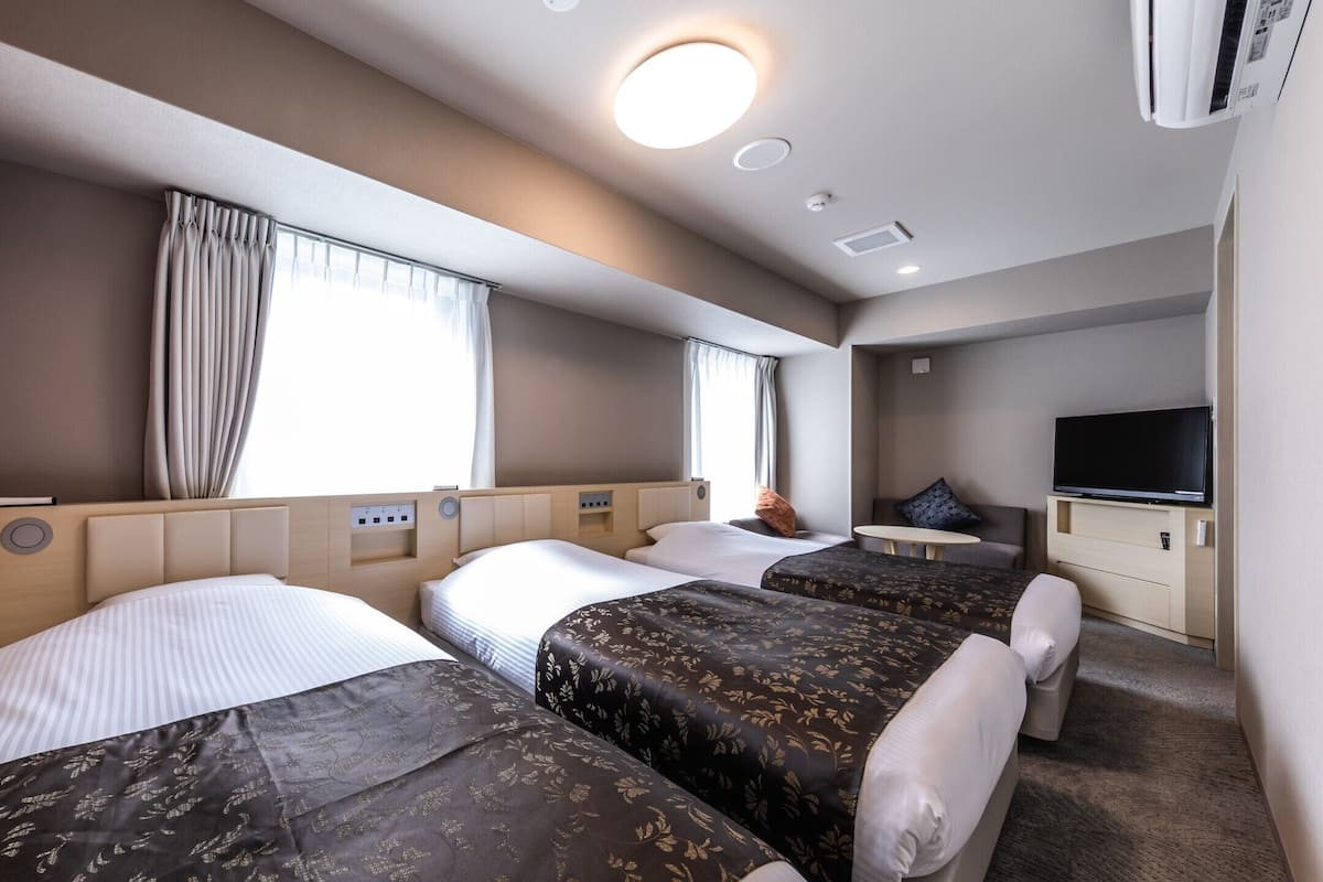 Une chambre d’hôtel avec trois lits, une télévision et un petit coin salon.