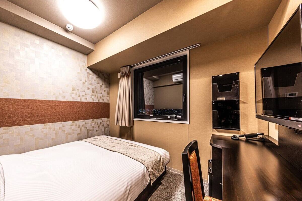 Une chambre d’hôtel avec un lit, une télévision, un miroir et une fenêtre avec des rideaux.