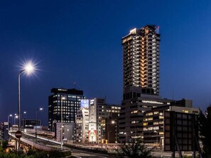 Ein Hochhaus mit mehreren Etagen und Balkonen, umgeben von anderen Gebäuden und einer belebten Straße mit fließendem Verkehr.