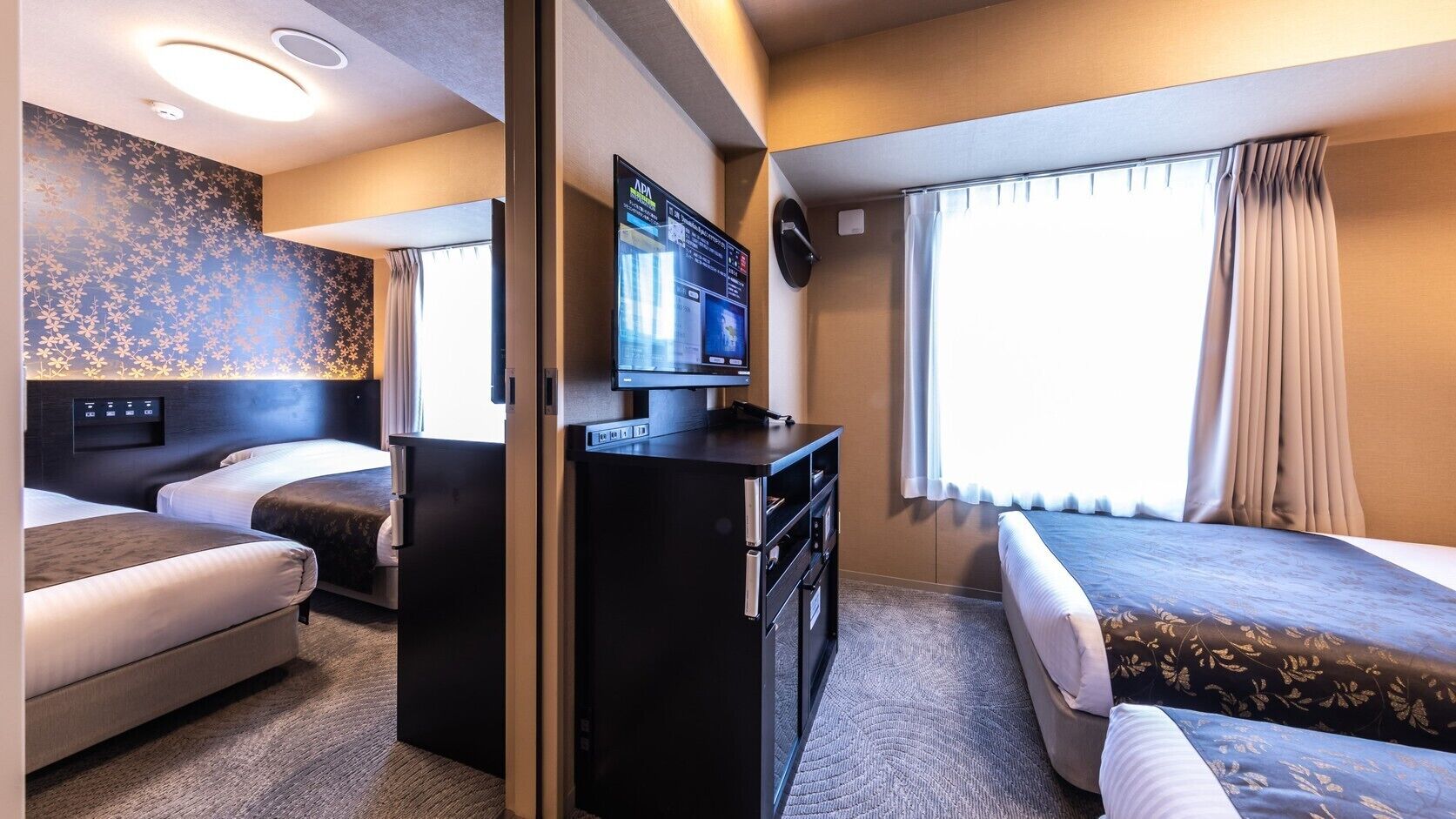 Une chambre d’hôtel avec deux lits, un bureau doté d’un téléviseur à écran plat, un panneau de commande fixé au mur et une fenêtre avec des rideaux.