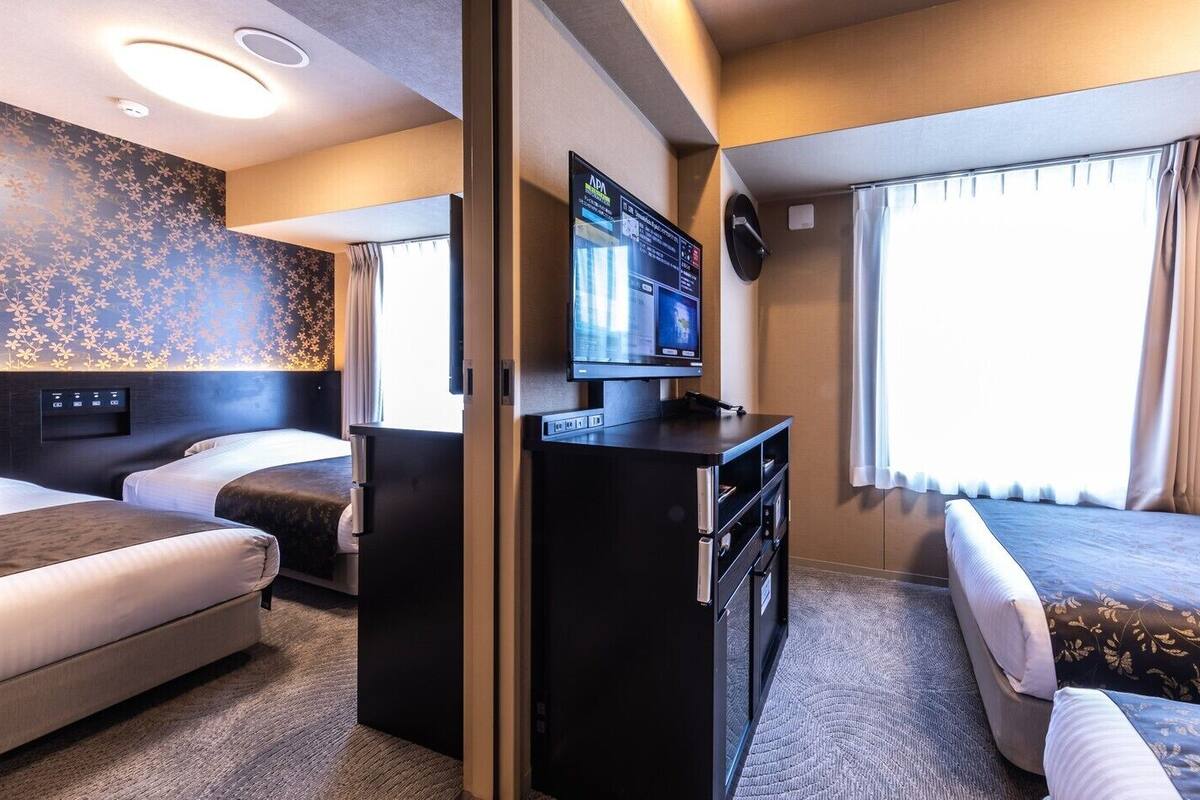 Une chambre d’hôtel avec deux lits, un bureau doté d’un téléviseur à écran plat, un panneau de commande fixé au mur et une fenêtre avec des rideaux.