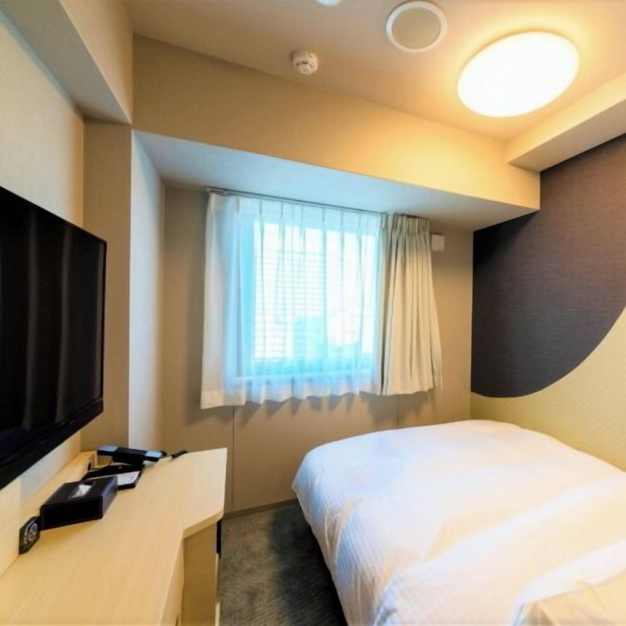 Ein Hotelzimmer mit Bett, Fernseher, Schreibtisch und einem fenster mit Vorhängen.