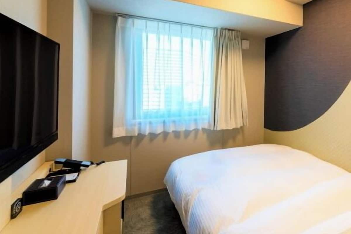 Une chambre d’hôtel avec un lit, une télévision, un bureau et une fenêtre avec des rideaux.