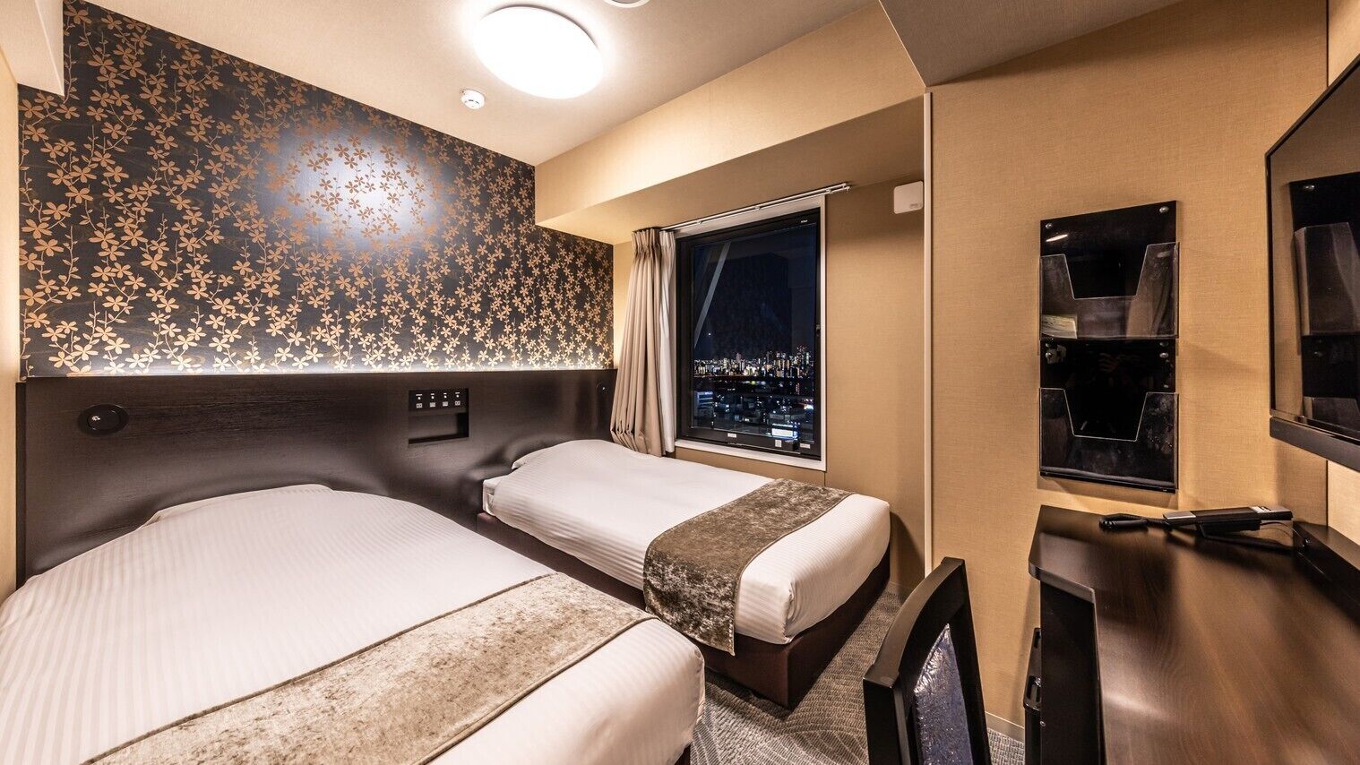 Une chambre d’hôtel avec deux lits, une grande fenêtre donnant sur la ville, un minibar et une télévision.