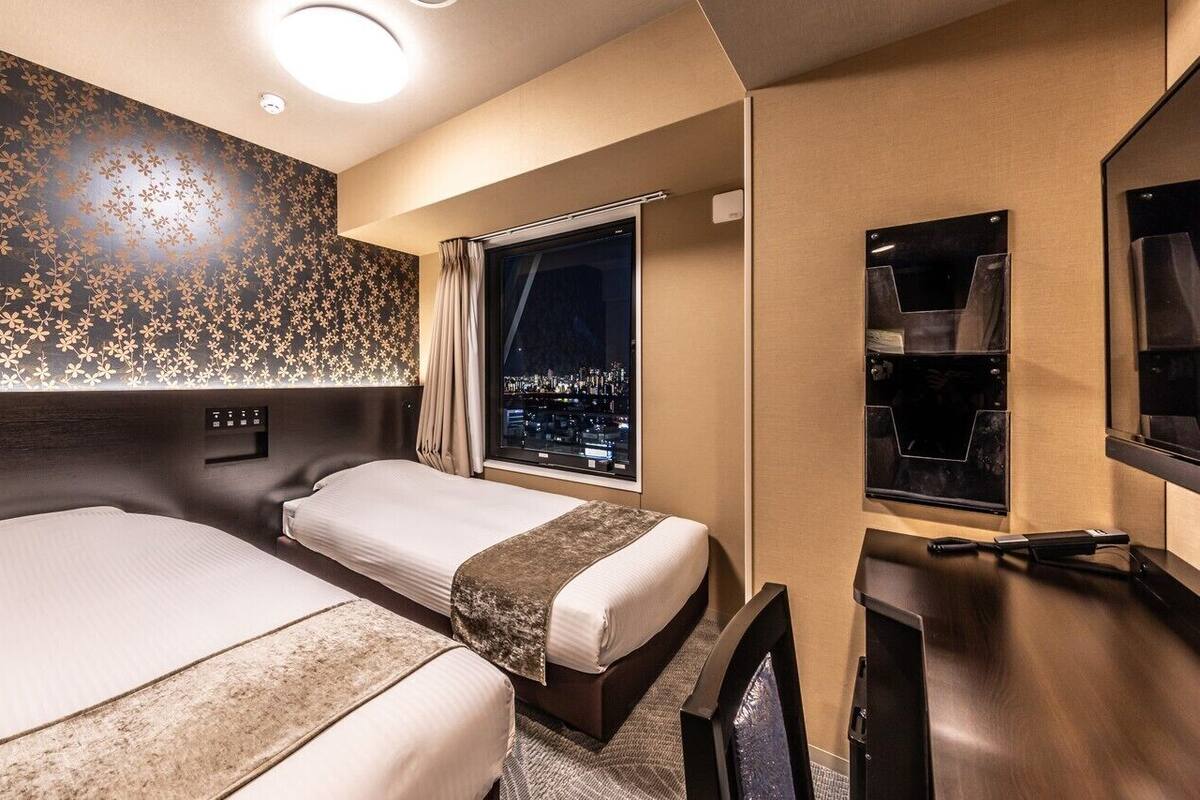 Une chambre d’hôtel avec deux lits, une grande fenêtre donnant sur la ville, un minibar et une télévision.