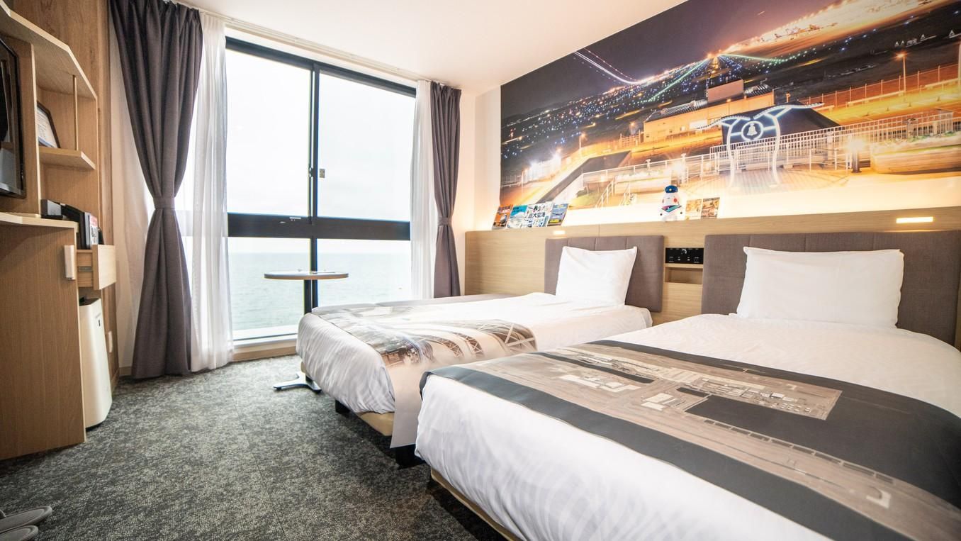 A hotel room with two beds, a large window, a view of a stadium, and a carpeted floor.