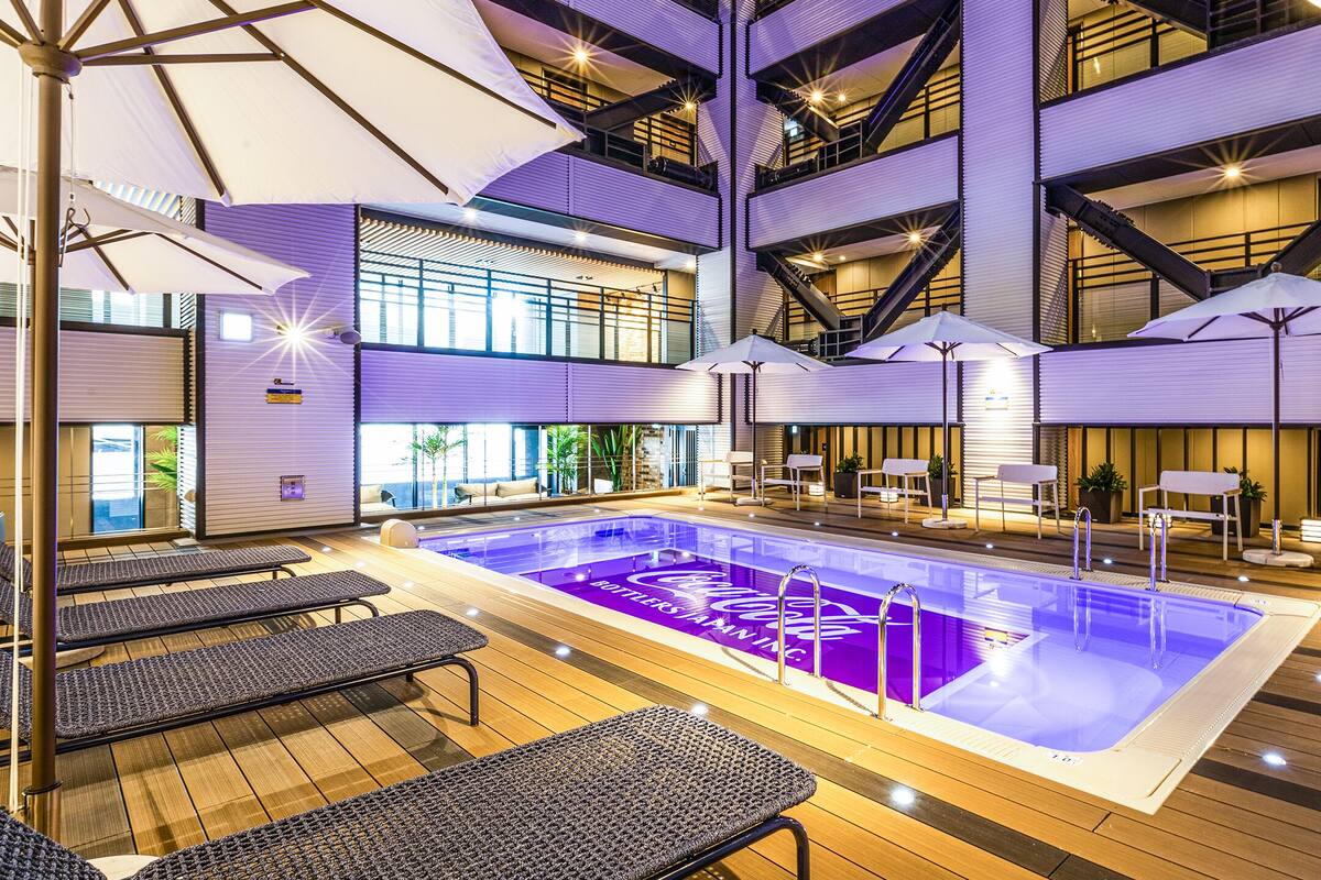 A modern indoor pool area with multiple levels, seating areas, and a Coca-Cola branding on the pool floor.