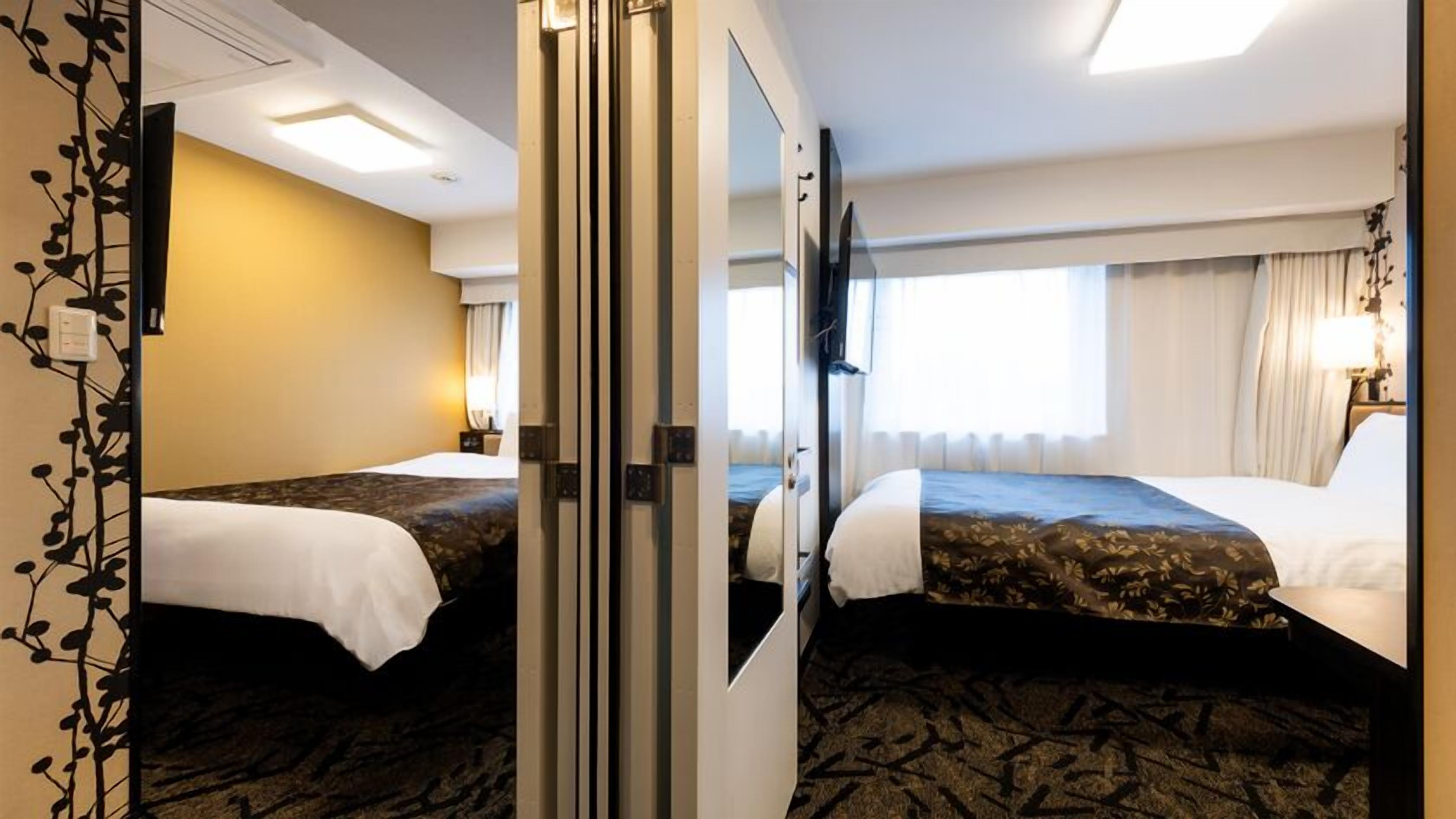 Ein Hotelzimmer mit zwei Betten, einem großen Spiegel, einem Flachbildfernseher und einem Fenster mit Vorhängen.