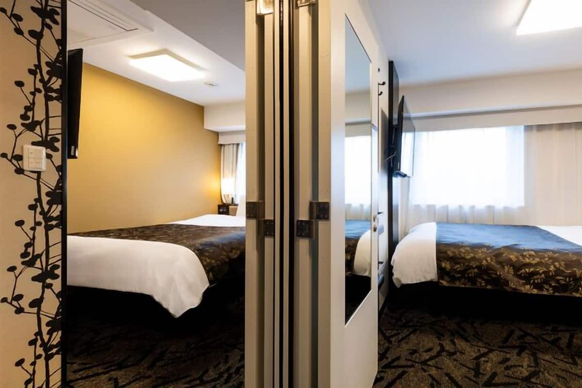 A hotel room with two beds, a large mirror, a flat-screen TV, and a window with curtains.