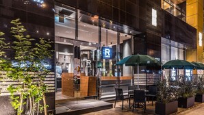 A modern building with a glass facade, outdoor seating area, and a visible sign for a cafe. - APA Hotel Resort Midosuji Hommachi Eki Tower (Osaka)