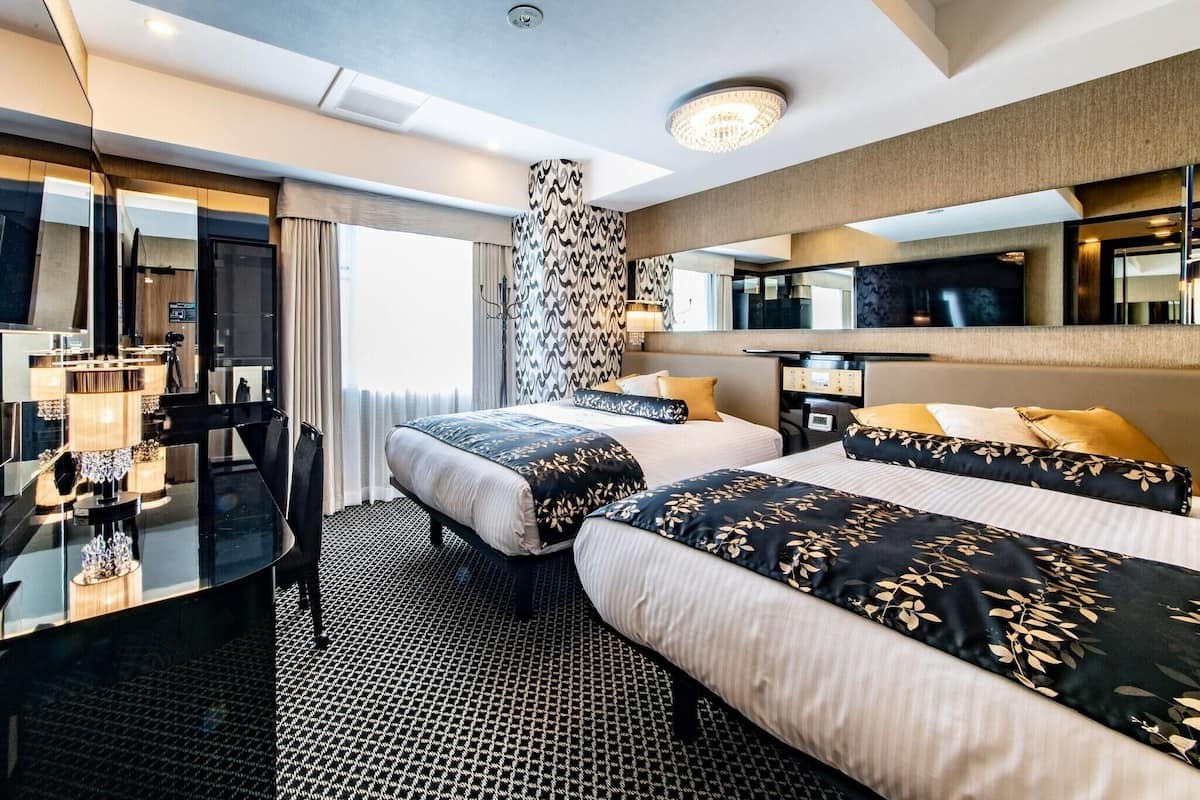 A hotel room with two beds, a desk, a chair, a TV, and a large mirror.