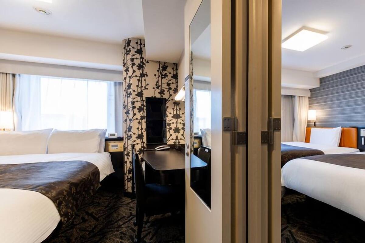 A hotel room with two beds, a desk, a chair, and a large window.