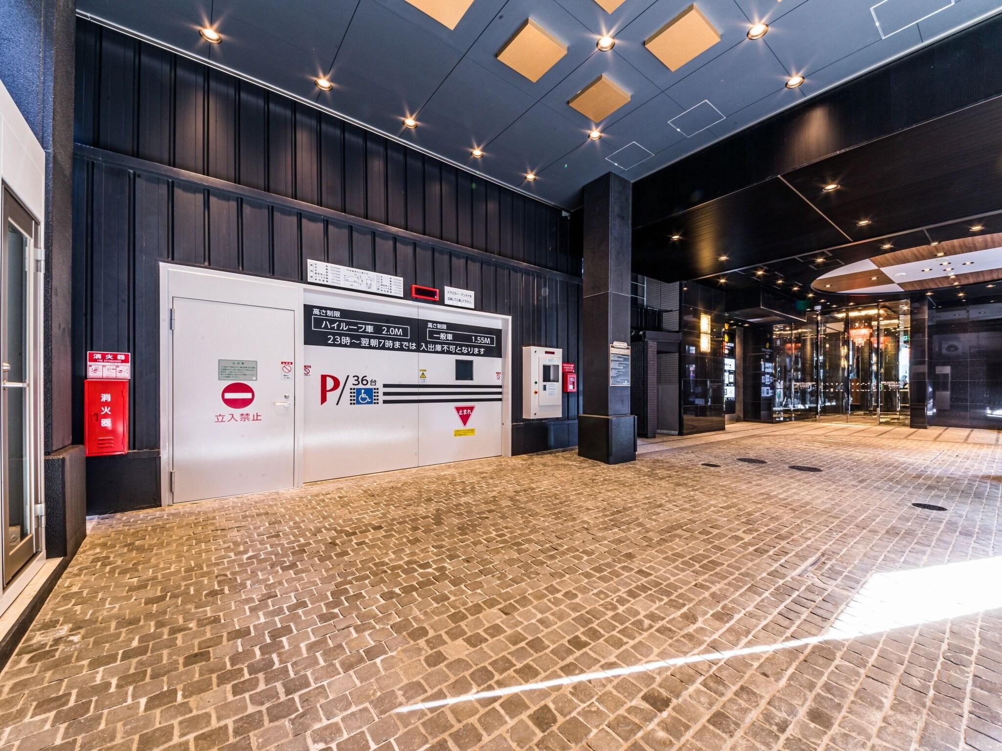 Entrada de hotel com piso de tijolos, placa de estacionamento e extintor de incêndio.