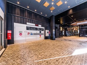 L’entrée d’un hôtel avec un sol en briques, un panneau indiquant l’emplacement du parking et un extincteur.