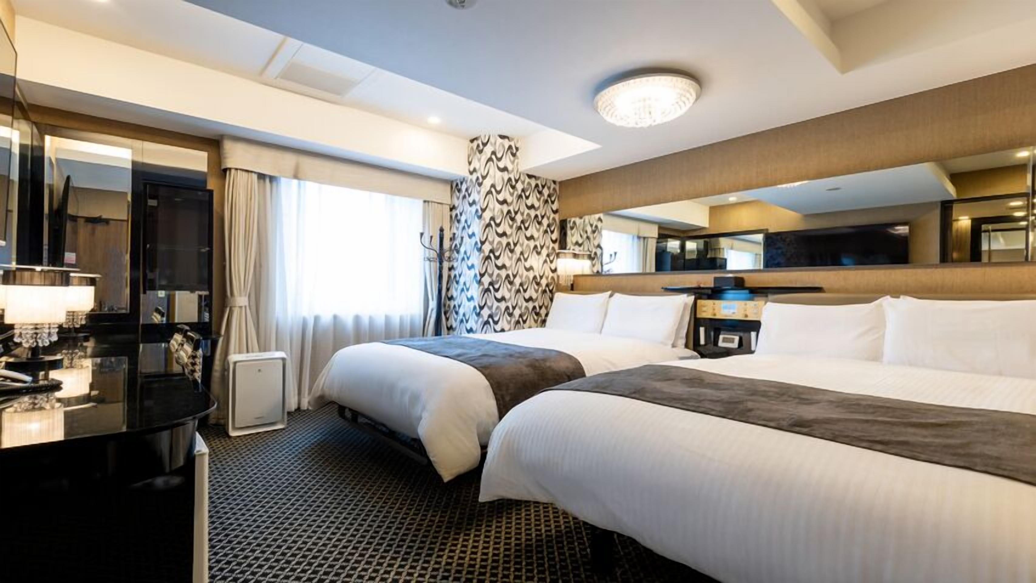 Ein Hotelzimmer mit zwei Betten, einem Schreibtisch, einem Spiegel und einem großen Fenster.