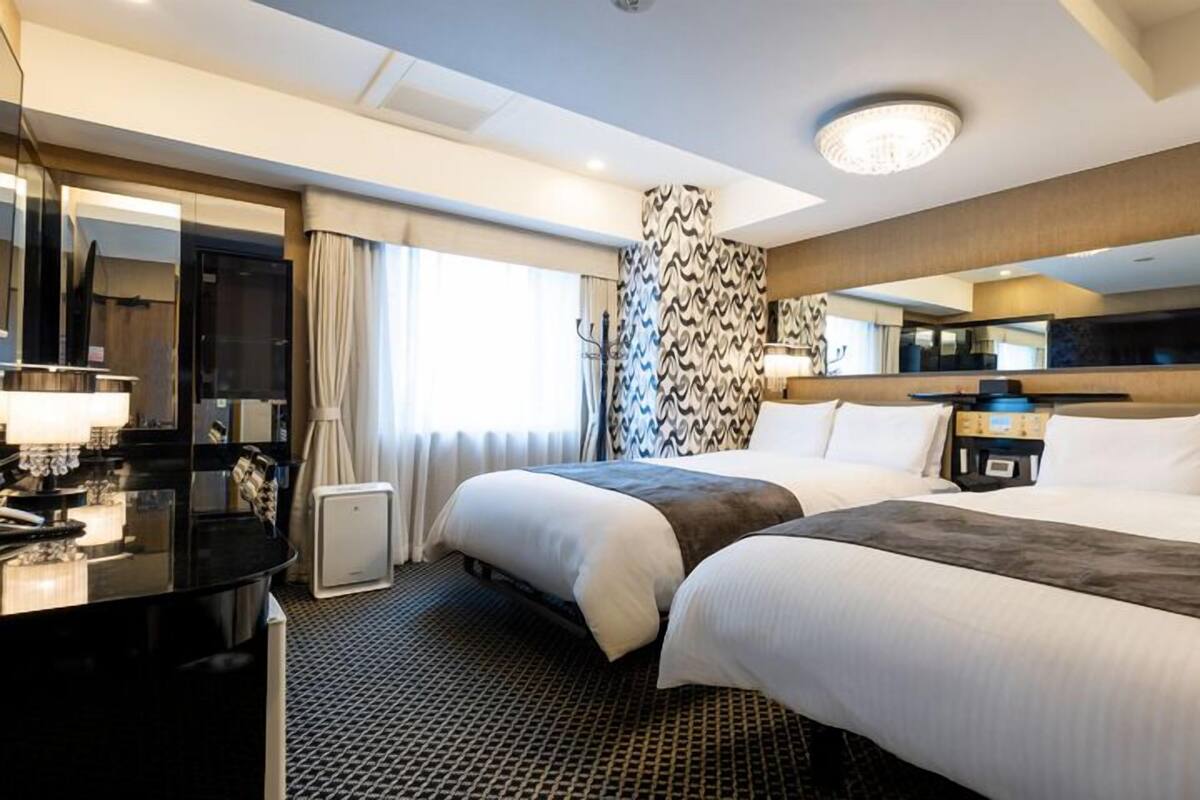 A hotel room with two beds, a desk, a mirror, and a large window.