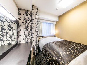 Une chambre d’hôtel avec un lit, un bureau, une chaise, une table de chevet et une fenêtre avec des rideaux.