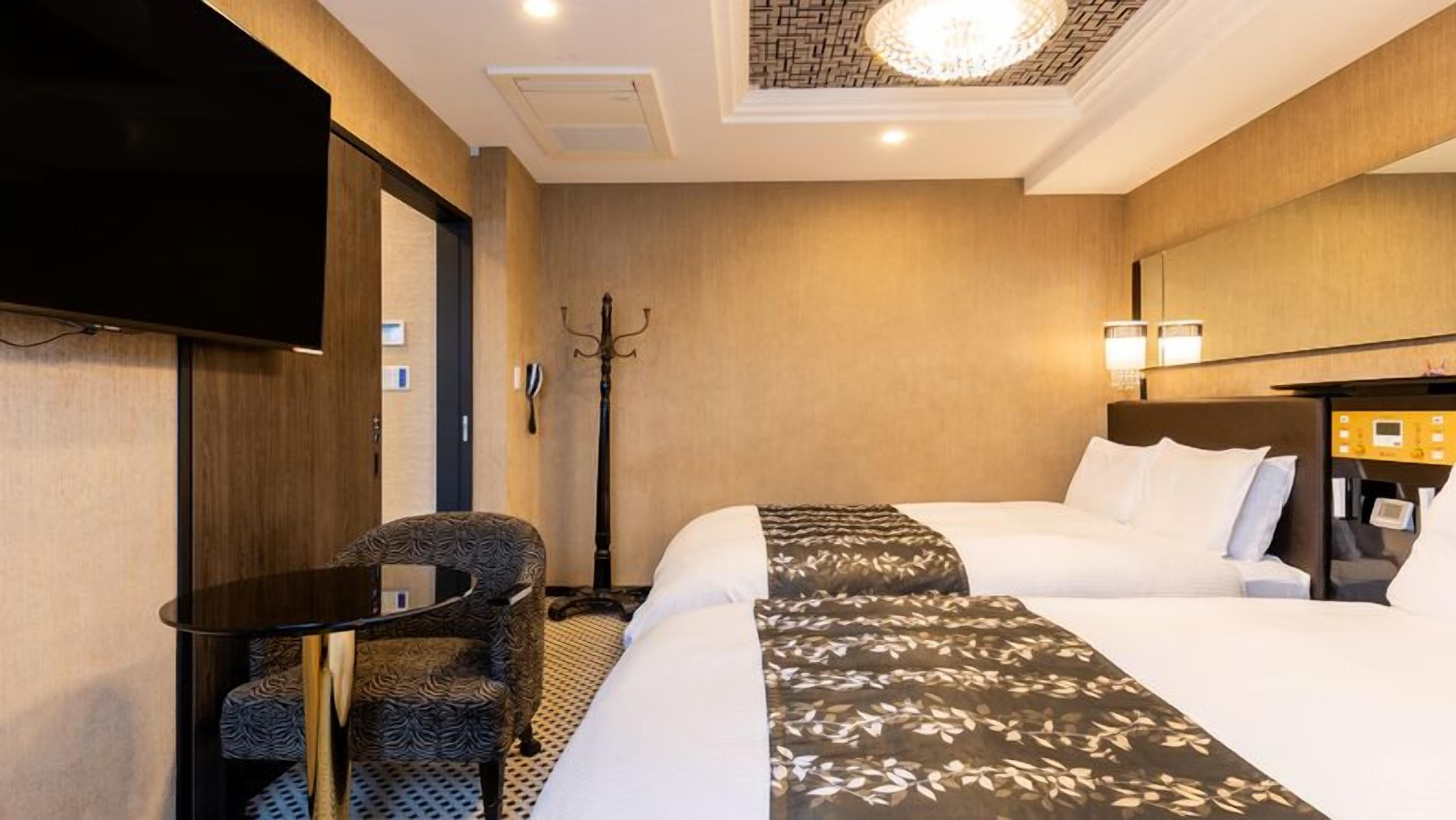 Ein Hotelzimmer mit Bett, Schreibtisch, Stuhl, Fernseher, Kleiderhaken und Deckenleuchte.