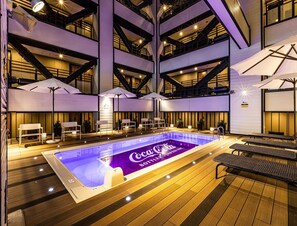 Un espace piscine intérieur à plusieurs niveaux, doté de coins salon et de parasols, et arborant le logo Coca-Cola sur le fond de la piscine.