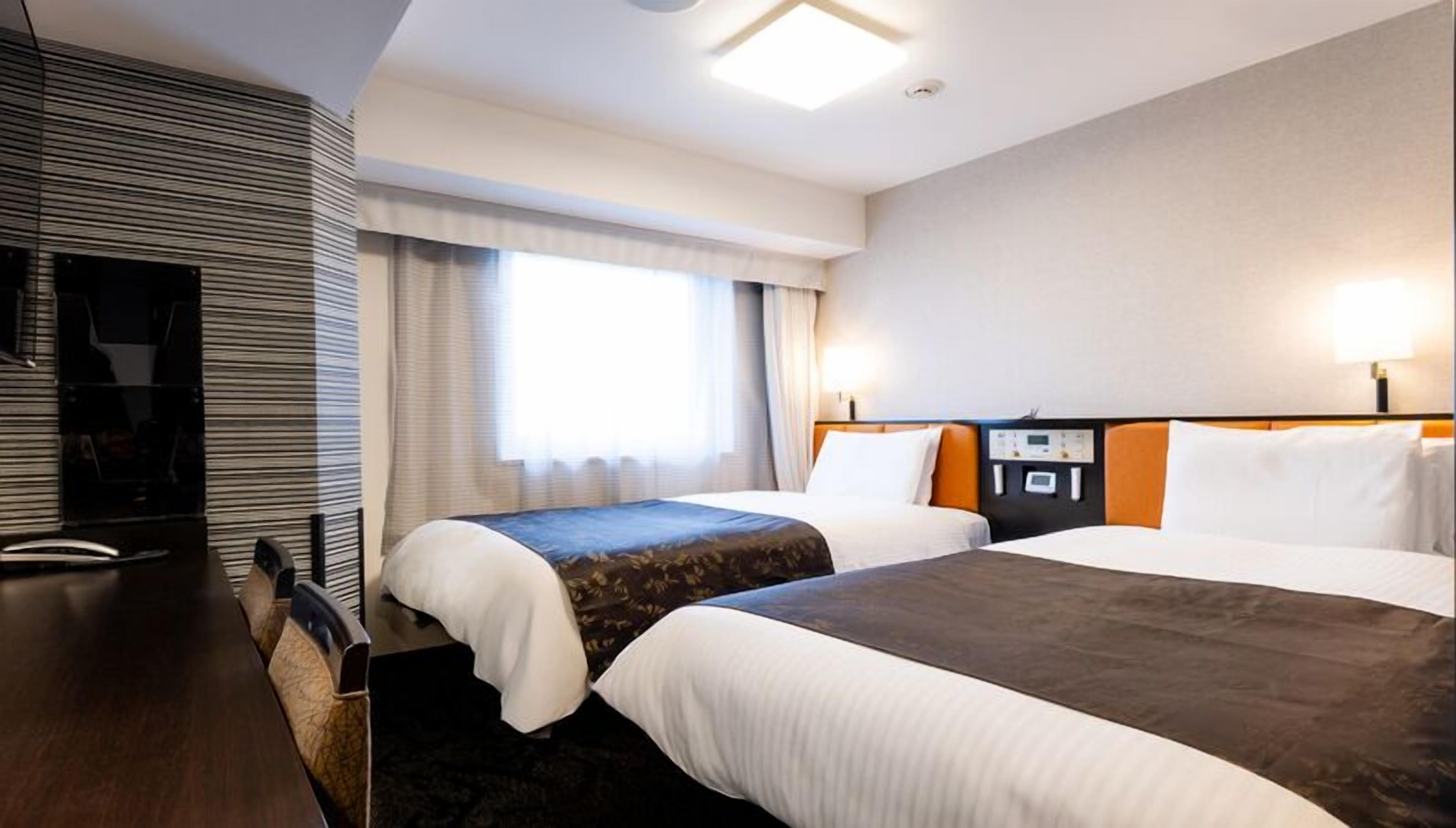 Ein Hotelzimmer mit zwei Betten, einem Schreibtisch und einem großen Fenster.