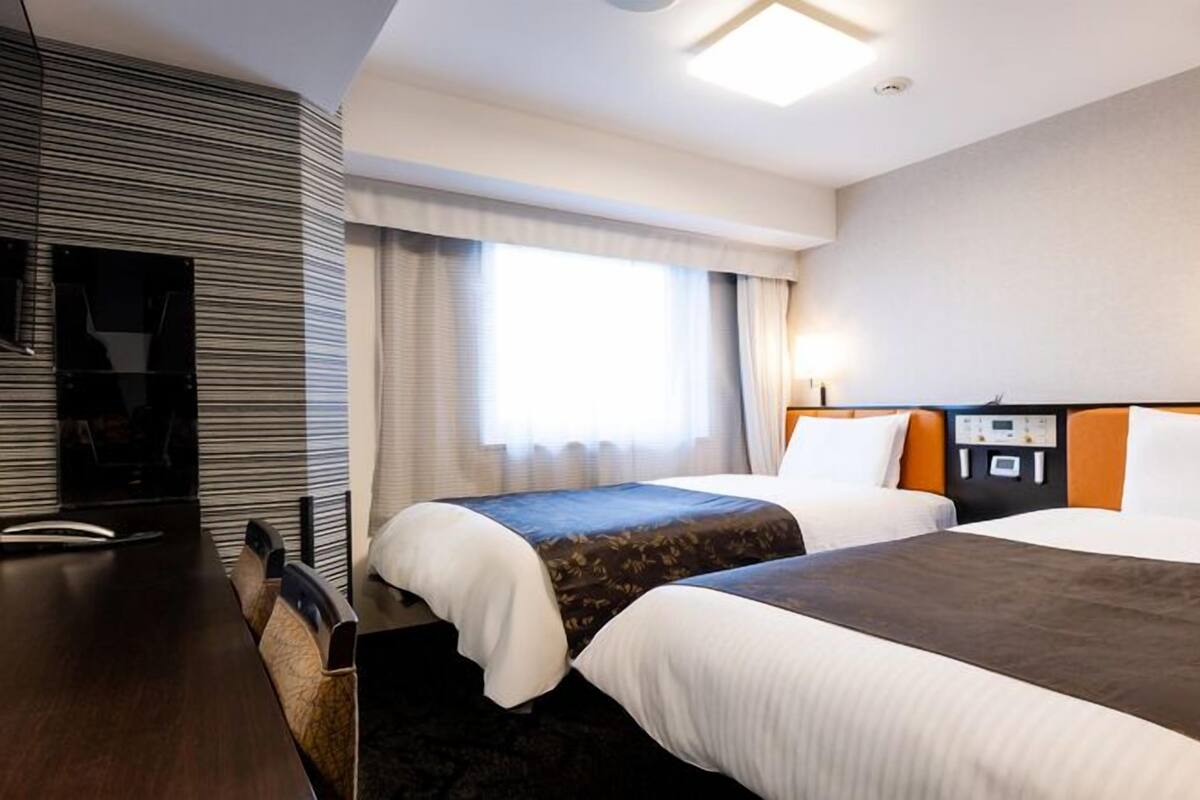 A hotel room with two beds, a desk, and a large window.