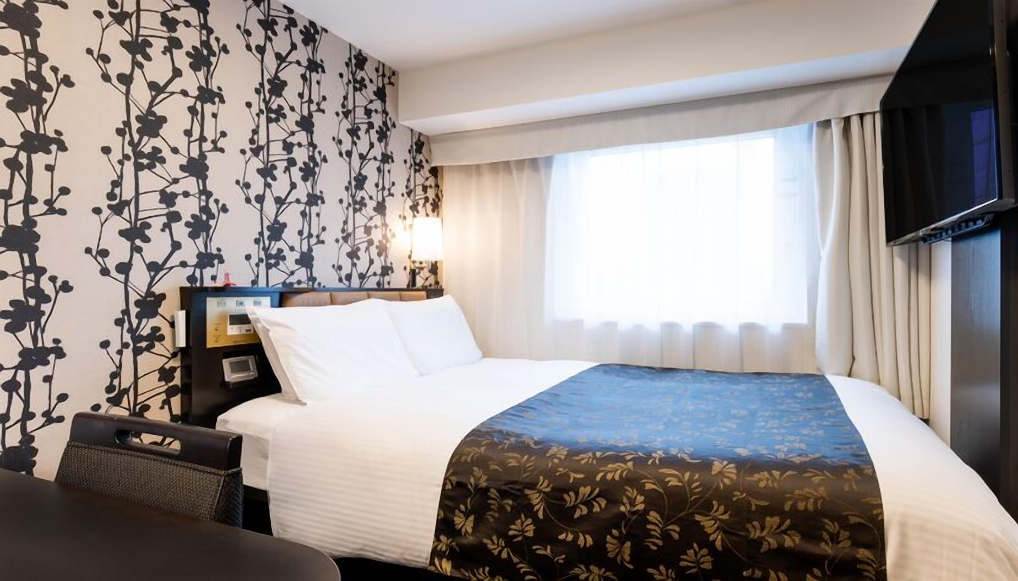Ein Hotelzimmer mit Bett, Schreibtisch, Fernseher und einem Fenster mit Vorhängen.
