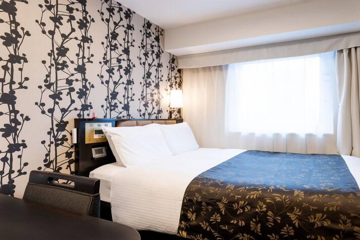 A hotel room with a bed, a desk, a TV, and a window with curtains.