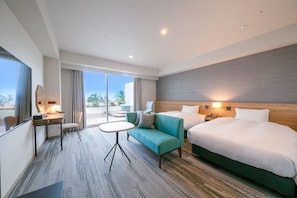 Habitación de hotel con una cama grande, un sofá, un escritorio con una silla y una mesita. Se ve un ventanal con vistas a palmeras.
