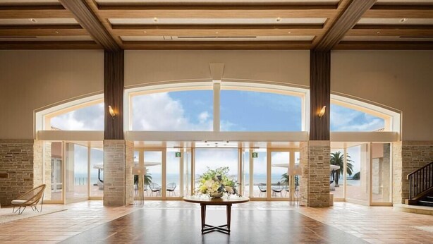 A spacious lobby with a high ceiling, large windows, and a central table with a floral arrangement. - Sunshine Sazan Seto (Suooshima)