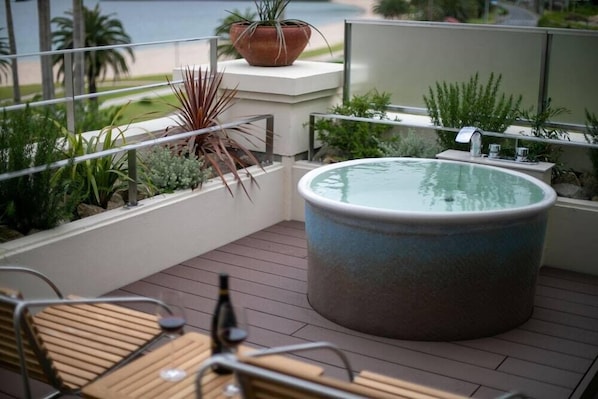 Un balcón con jacuzzi, zona de estar y plantas en macetas.