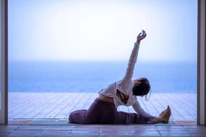 Una persona che esegue una posa yoga su un tappetino in una stanza con vista sull'oceano.