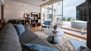 A modern living room with a large sofa, a coffee table, and a bookshelf. There is a balcony with a view of the ocean. - Sunshine Sazan Seto (Suooshima)