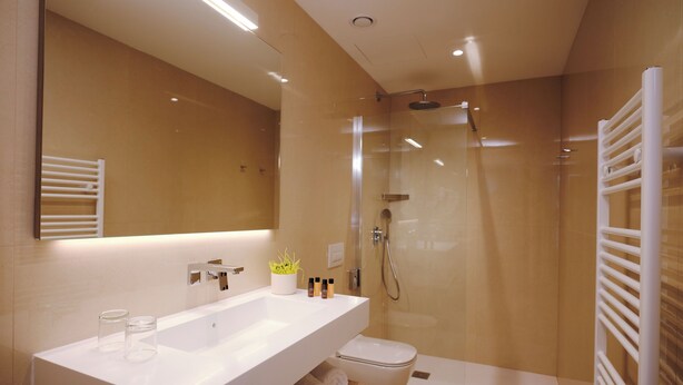 Un baño moderno con un espejo grande, un tocador blanco, ducha con cerramiento de vidrio y un inodoro blanco.