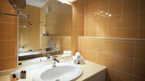 Un baño con un lavamanos blanco, un espejo y paredes de azulejos anaranjados.