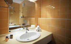 Un bagno con lavandino bianco, specchio e pareti rivestite di piastrelle arancioni.