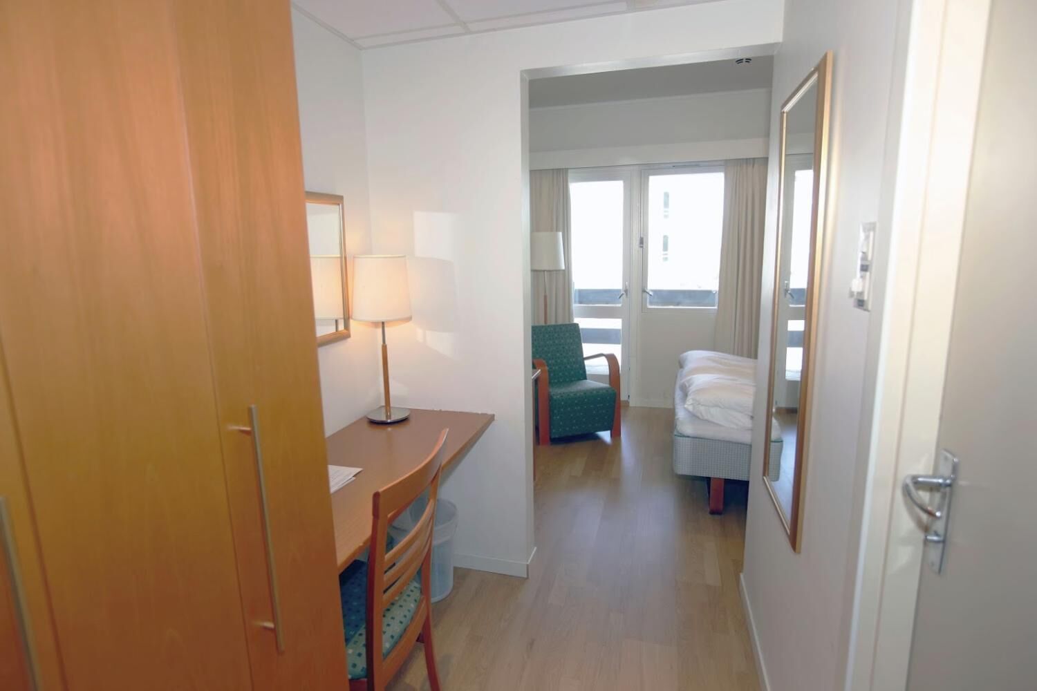 A hotel room with a desk, chair, bed, and a window with curtains.