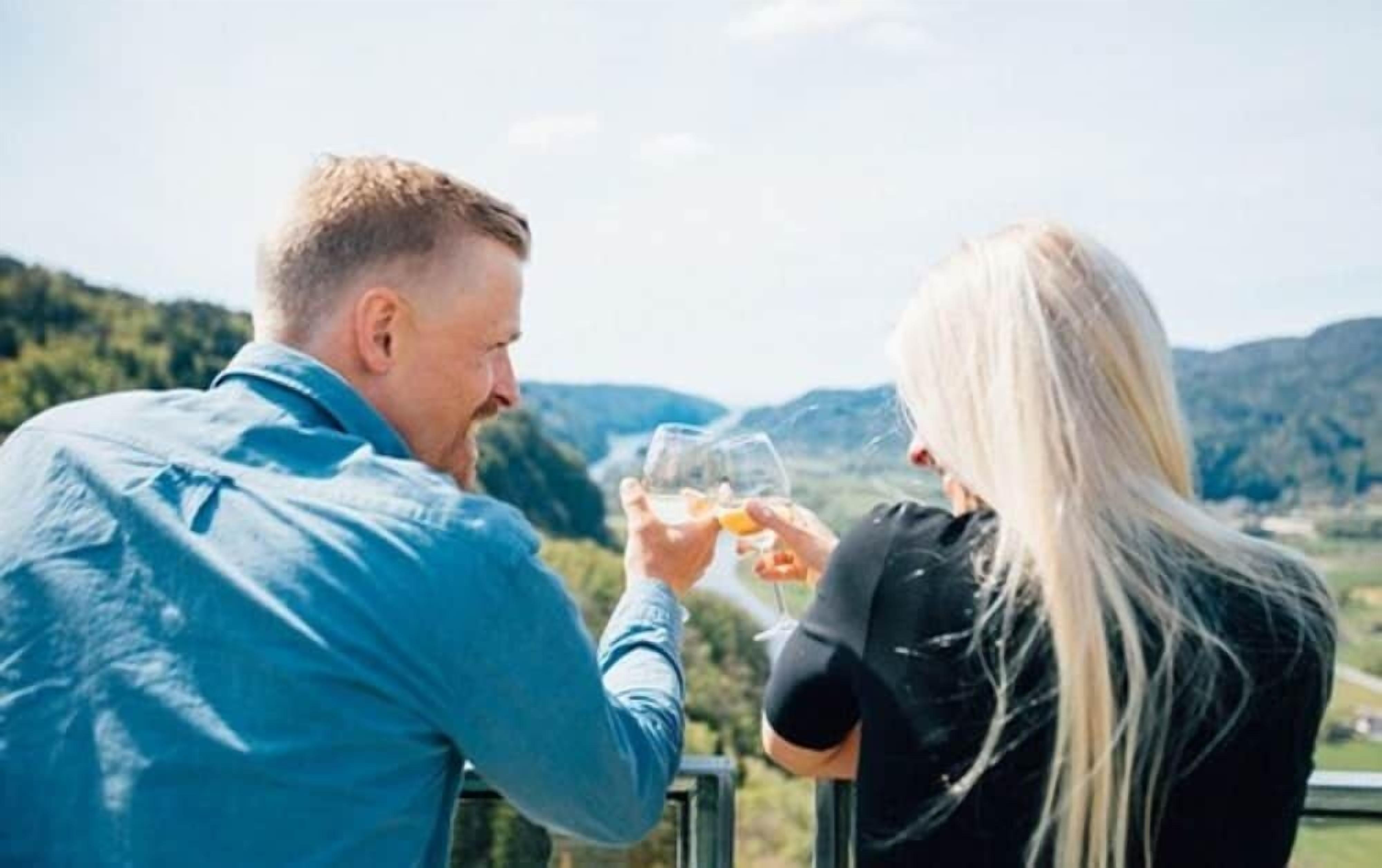 Two people toasting with wine glasses against a scenic mountain backdrop.