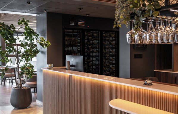 A reception area with a modern design, featuring a reception desk, a potted plant, and a wine rack in the background.