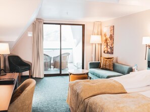 A hotel room with a bed, a desk, a chair, a sofa, and a balcony with outdoor furniture. - Ullensvang (Ullensvang)