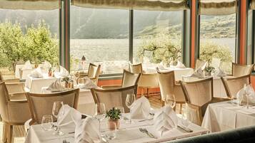 A restaurant with tables set for dining, overlooking a body of water and hills.