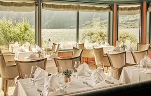 A restaurant with tables set for dining, overlooking a body of water and hills.