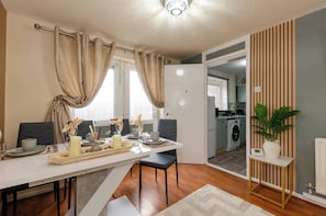 Uma cozinha moderna com máquina de lavar roupa, uma área de refeições com mesa posta para dois e um vaso de plantas.