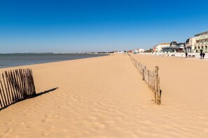 Een zandstrand met een houten omheining en gebouwen op de achtergrond.