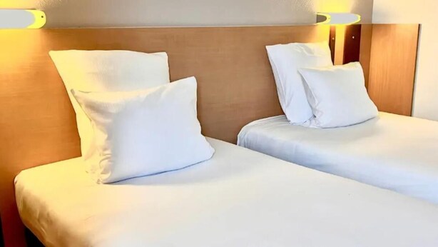 Ein Hotelzimmer mit zwei Betten, jeweils mit weißer Bettwäsche und Kissen, und einem Holz-Kopfschild.