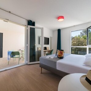 Hotelkamer met een bed, een bureau, een stoel, een televisie en een schuifdeur naar een buitenruimte.
