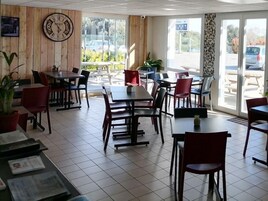 A restaurant with multiple tables and chairs, a clock on the wall, and large windows with a view of the outside.