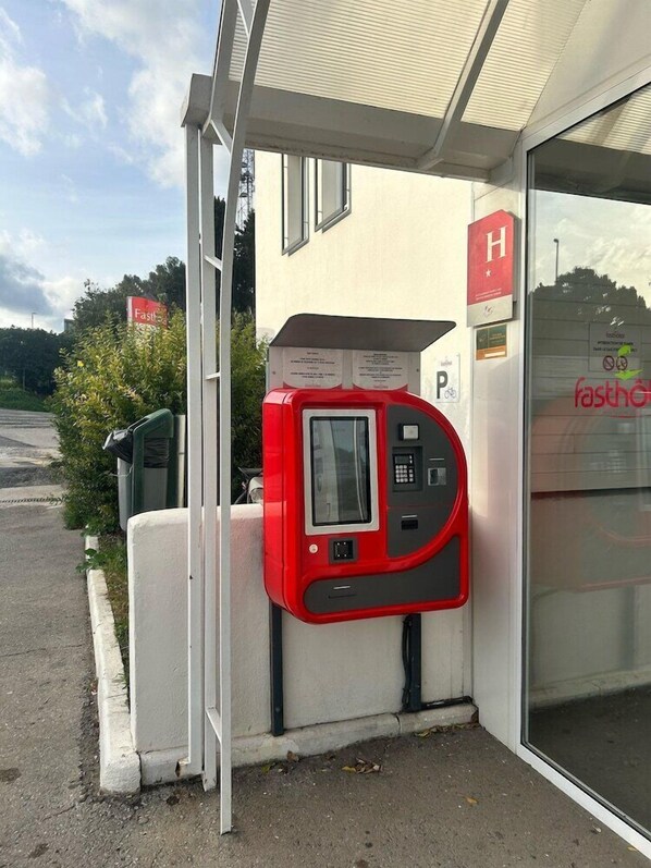 Ein rotes Parkgerät vor einem Gebäude, an dem ein Schild mit dem Schriftzug „Fastfood“ hängt.