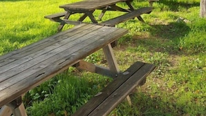 Due tavoli da picnic in legno in un prato con alberi e un edificio sullo sfondo.